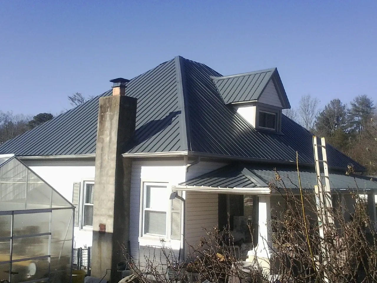 Dark blue standing seam metal roof on a white farmhouse with dormer — Slate & Tile Roof Repair by Roofing Brothers in Roundhill
