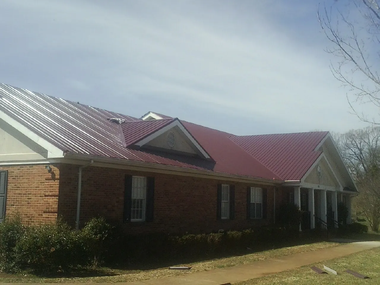 Red metal roof with gabled entries on a long brick building, from a Hail Damage Roof Repair job in Roundhill