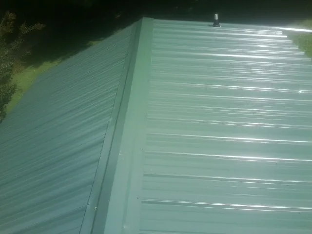 New green metal panels meeting at the ridge of a roof — Flat Roof Repair work by our crew in Roundhill