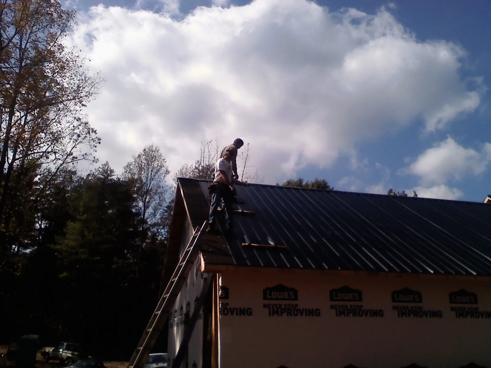 Roofer fastening dark metal panels high against a cloudy sky, from a Roof Inspection job in Roundhill